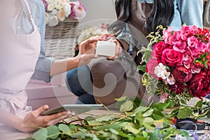 Young florists holding blank white card and using digital tablet in flower shop