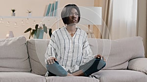 Young focused african american woman sitting in lotus position with closed eyes healthy calm girl relaxing on sofa