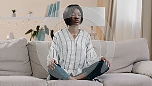 Young focused african american woman sitting in lotus position with closed eyes healthy calm girl relaxing on sofa