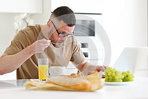 Young focused handsome man working remotely on laptop in modern kitchen at home