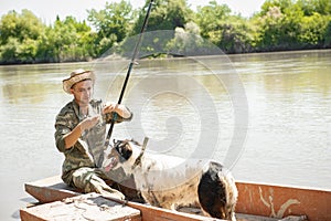 Young focused male angler putting bait on hook, while sitting in old wooden boat and fishing.