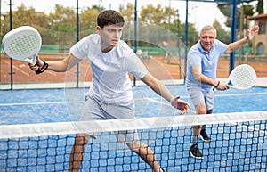 Young focused man playing doubles paddle tennis