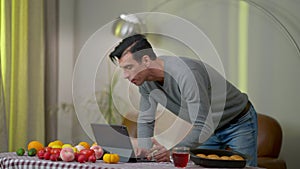 Young focused Middle Eastern man watching online recipe on tablet standing at table with fruits and vegetables