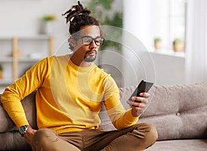 Young focused serious african american man relaxing at home with smartphone, surfing internet