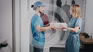 Young food delivery man in a blue uniform. A man brought pizza and a bag of food to a beautiful woman.