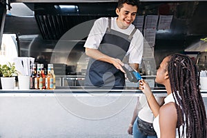Young food truck owner receiving payment through credit card from a female customer