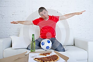 Young football fan man watching game on tv in team jersey celebrating goal crazy happy on couch