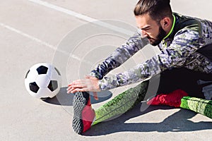 Young footballer stretching legs sitting at floor
