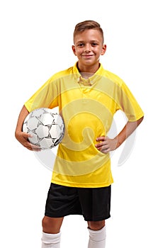 A young footballer in a yellow t-shirt and black shorts holds in arms a ball isolated on a white background.