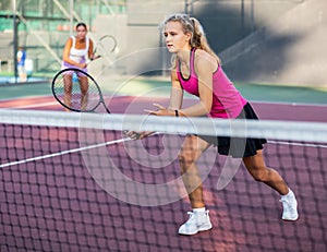 Young forcefully teenage girl playing tennis close to net on court