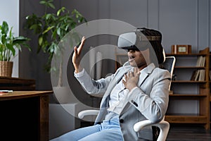 Young formal business woman use virtual reality glasses scared, stretches out hands sit in office