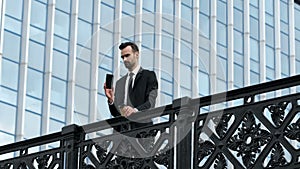 A young and free man with coffee and a smartphone stands at the bridge railing.