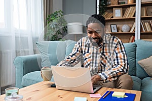 Young freelance business man or exchange student working remotely from his home office on laptop computer. African American work