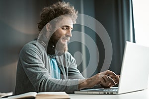 Young freelancer man working at laptop sitting at the desk at home office and making notes or programming as IT