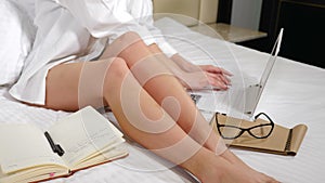 Young freelancer woman enjoying morning in hotel apartment. Close up of Girls legs on white beddings. Working atmosphere