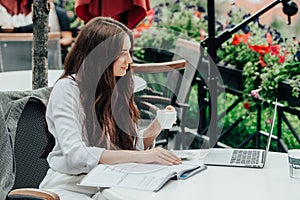 Young freelancer woman using laptop computer sitting at cafe table. Smiling woman working online or studying and