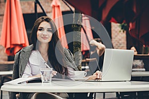 Young freelancer woman using laptop computer sitting at cafe table. Smiling woman working online or studying and