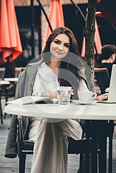 Young freelancer woman using laptop computer sitting at cafe table. Smiling woman working online or studying and