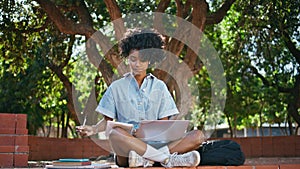 Young freelancer writing notes in notepad sitting park with laptop. Girl webinar