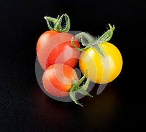 A young fresh beautiful yellow cherry tomato and two very small ripe red cherry tomatoes on a glossy black background with reflect