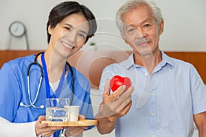 Young friendly asian female caregiver look at camera to happy senior man in nursing home