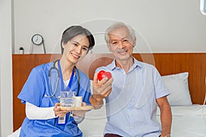 Young friendly asian female caregiver look at camera to happy senior man in nursing home