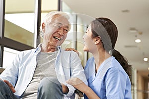 Young friendly asian female caregiver talking to elderly man in nursing home