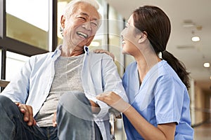 Young friendly asian female caregiver talking to elderly man in nursing home photo