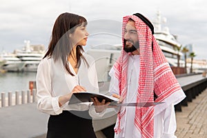 Young friendly europian businesswoman explaning contract details to arab man during meeting in port