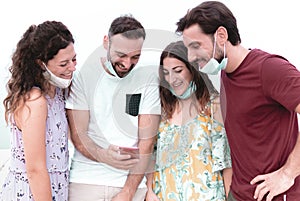 Friendly young man having fun with smartphone - happy group enjoying free time wearing surgical mask