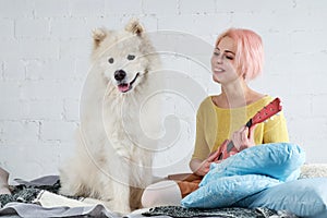 young friendly joyful girl playing the ukulele, the guitar sitting on the couch with her friend a big white dog.