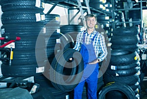 Young friendly mechanic man working with car tires in workshop