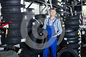 Young friendly mechanic man working with car tires in workshop