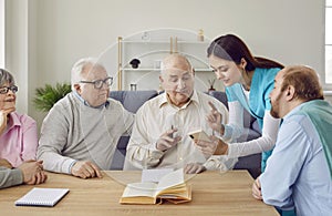 Young friendly nurse helping senior people with mobile phone in nursing home