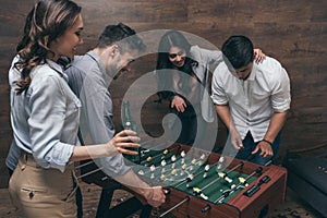 Young friends drinking beer and playing foosball indoors