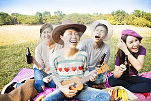 young friends enjoying picnic and playing ukulele