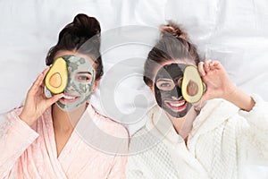 Young friends with facial masks  fun on bed at pamper party, top view