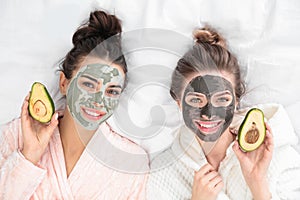 Young friends with facial masks having fun on bed at pamper party