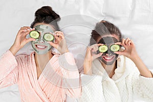 Young friends with facial masks having funon bed at pamper party, top view