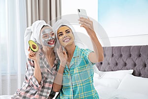 Young friends with facial masks taking selfie in bedroom