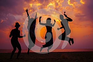 Young friends having fun on the beach and jumping against a backdrop of a sunset over the sea