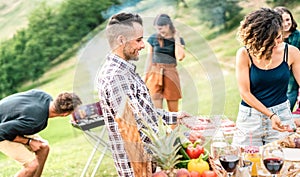 Young friends having fun on outdoors picnic preparing food at barbecue grill party - Happy people cooking and eating