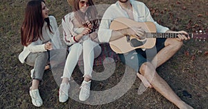 Young friends having picnic in the park, smiling and playing guitar.