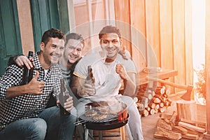 Young friends making barbecue and drinking beer on porch with back light