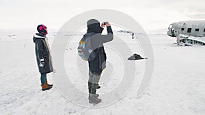 young friends near crashed airplane in Iceland taking pictures of the plane on the phones camera