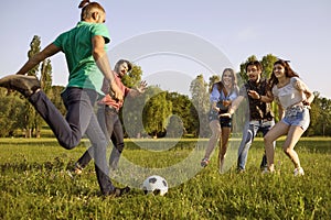 Young friends playing football game on green meadow. Students having fun on summer weekend in nature