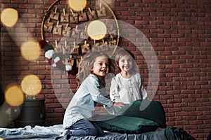Young friends resting together. Little girls having fun on the bed with holiday interior at the background