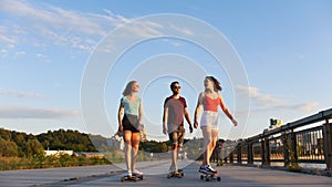 Young friends riding skateboards on the waterfront on a background of modern buildings - sunset
