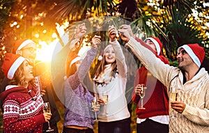 Young friends with santa hats celebrating Christmas with champagne wine toast outdoors - Tropical holidays concept