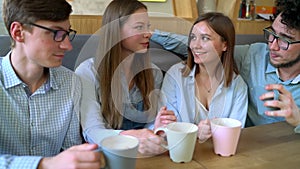 Young friends sit in a cafe, drink coffee and have fun communicating